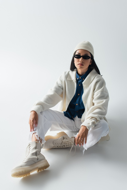 asian woman in white clothes and dark sunglasses looking at camera while sitting on grey - Fotoğraf, Görsel