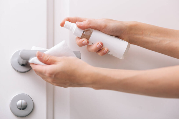 Cleaning white door handles with an antiseptic wet wipe and sanitizer spray. Disinfection in hospital and public spaces against corona virus. Woman hand using towel for cleaning home room door link - 写真・画像