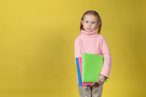 Portrait of attractive elementary age school girl on yellow background holding books - Фото, изображение