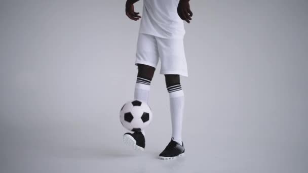 Um jogador profissional de futebol preto em um uniforme branco em um fundo branco faz malabarismos com uma bola em câmera lenta. Jogador de futebol étnico afro-americano com bola de futebol - Filmagem, Vídeo
