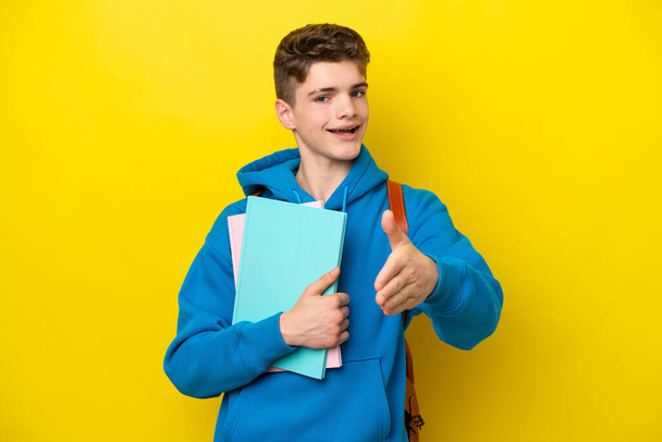 Teenager russischer Student Mann isoliert auf gelbem Hintergrund schüttelt Hände für den Abschluss eines guten Deals - Foto, Bild
