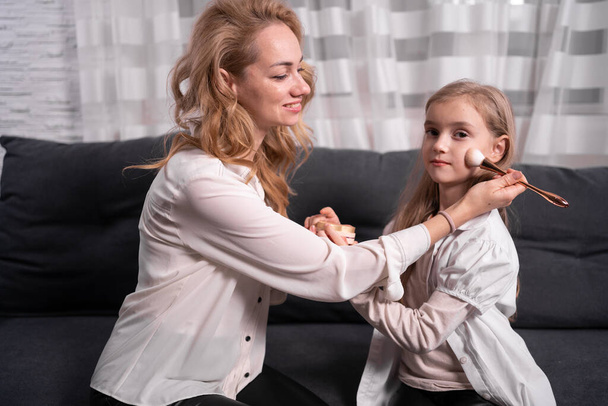 Happy loving family. woman and girl make up and have fun sitting at dressing table at home. child learn to use face powder mom helps. copy space. - Photo, Image