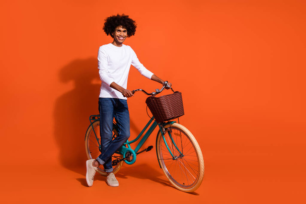 Photo of cute funky guy dressed white shirt riding bike empty space isolated orange color background. - 写真・画像