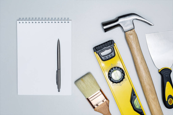 Différents outils de construction et cahier sur surface grise. Vue de dessus. J'écris le plan de travail. Concept de bricolage. - Photo, image