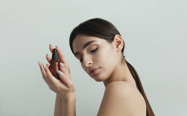 beautiful brunette holding face serum in her hands - Fotó, kép