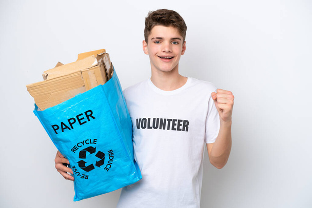 白地に隔離された紙をリサイクルするためにリサイクルバッグを持っている10代のロシア人男性勝者の位置で勝利を祝う - 写真・画像
