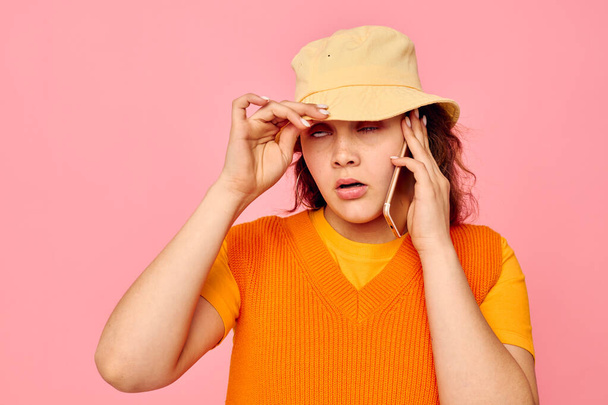 mujer bonita se comunica por teléfono en el sombrero amarillo de la moda de fondo rosa inalterado - Foto, imagen