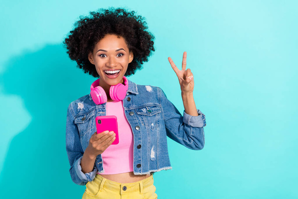 Photo of charming excited young woman wear jeans jacket headphones typing device v-sign isolated turquoise color background. - Fotoğraf, Görsel