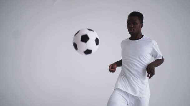 Een professionele zwarte voetballer in een wit uniform op een witte achtergrond jongleert in slow motion met een bal. Afro-Amerikaanse etnische groep voetballer met een voetbal - Video