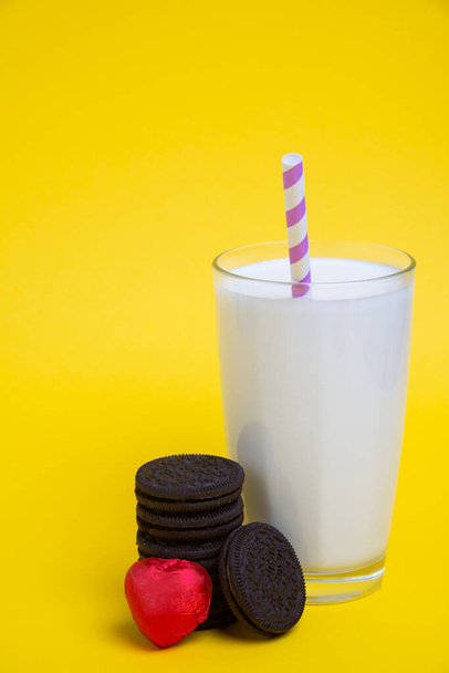 koekjes en hartvormige snoep voor Valentijnsdag en een glas melk op een gele achtergrond - Foto, afbeelding