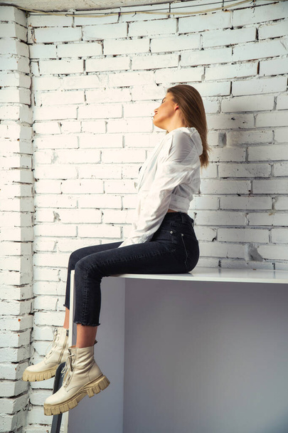 Foto de una joven hermosa mujer sensual y sexy con el pelo largo usando una camisa blanca posando contra una pared de ladrillo blanco en el estudio.   - Foto, Imagen