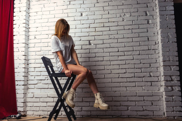 Kuva nuori kaunis aistillinen ja seksikäs nainen pitkät hiukset yllään t-paita poseeraa valkoista seinää vasten studiossa.   - Valokuva, kuva