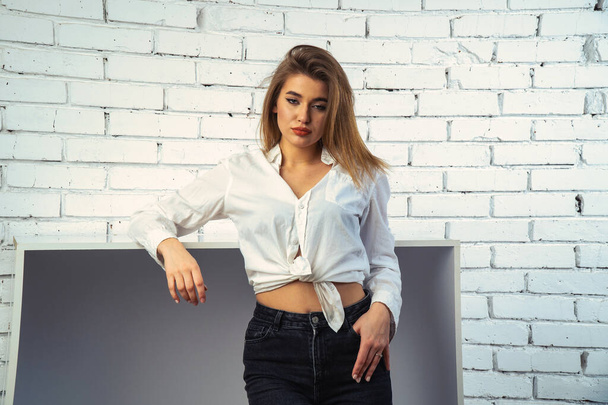 Stüdyoda beyaz gömlekli seksi ve seksi bir kadının beyaz bir duvara poz verdiği bir fotoğraf..   - Fotoğraf, Görsel