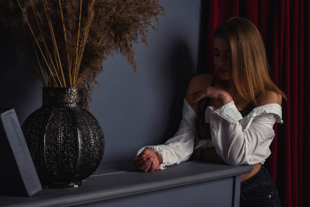 Foto de una joven hermosa sensual y sexy mujer con el pelo largo usando una camisa blanca posando junto al piano en el estudio.   - Foto, Imagen