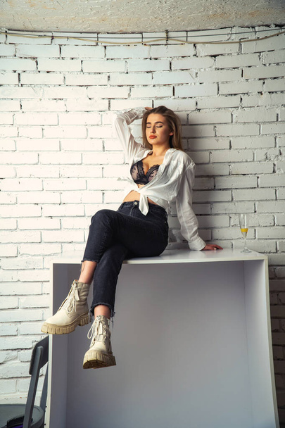 Foto de jovem bela sensual e sexy mulher com cabelos longos vestindo em camisa branca posando contra uma parede de tijolo branco no estúdio.   - Foto, Imagem