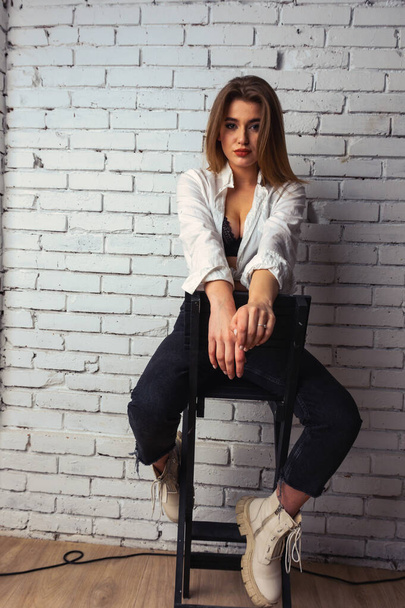 Photo of young beautiful sensual and sexy woman with long hair wearing in white shirt posing against a white brick wall in the studio.   - Foto, Bild