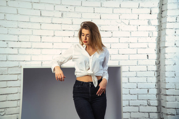 Foto von jungen schönen sinnlichen und sexy Frau mit langen Haaren trägt in weißem Hemd posiert vor einer weißen Ziegelwand im Studio.   - Foto, Bild