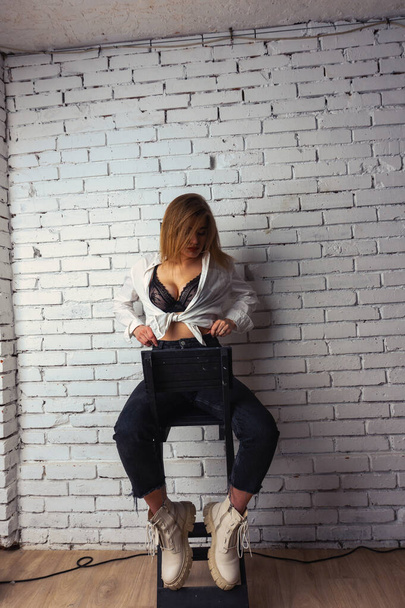 Foto mladé krásné smyslné a sexy ženy s dlouhými vlasy na sobě v bílé košili pózuje proti bílé cihlové zdi ve studiu.   - Fotografie, Obrázek