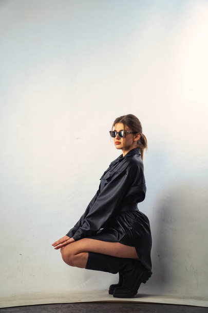 Photo of young beautiful sensual and sexy woman with long hair wearing in black shirt posing and sunglasses against a white wall in the studio.   - Φωτογραφία, εικόνα