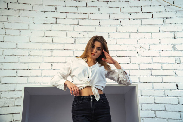 Photo of young beautiful sensual and sexy woman with long hair wearing in white shirt posing against a white brick wall in the studio.   - 写真・画像