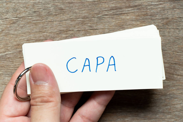 Hombre mantenga la tarjeta flash con la palabra de escritura CAPA (abreviatura de acción correctiva y acción preventiva) sobre fondo de madera - Foto, imagen