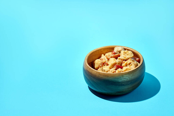 Stewed potatoes with meat and mushrooms in a wooden bowl on a blue background - Photo, image