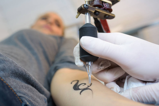 close up hands with machine doing tattoo on womans arm - Valokuva, kuva