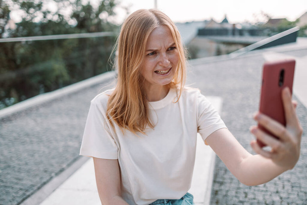 Städtische blonde Haare junge wütende Frau posiert draußen im Park machen ein Selfie mit dem Handy im Freien im Sommer. Depressive Abhängigkeit von sozialen Medien - Foto, Bild