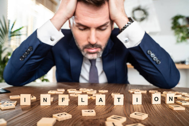 Worried businessman with the word inflation on the table. Supply-demand balance, market laws, economics and free commerce. Stock quotes movement - Zdjęcie, obraz