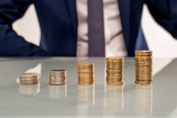 Stack of coins on a desks. Businessman in suit on the background. A lof of copy space. Investment. Economy. Finance. Savings. - Fotoğraf, Görsel
