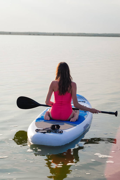 Young female paddle boarding at sunset. - Фото, изображение
