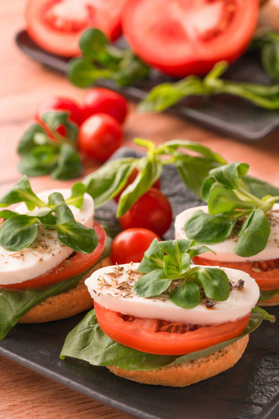 Image verticale de la salade italienne classique caprese avec des tomates tranchées, mozzarella et basilic sur bruschettas sur plaque noire sur fond de table en bois. Apéritif traditionnel - Photo, image