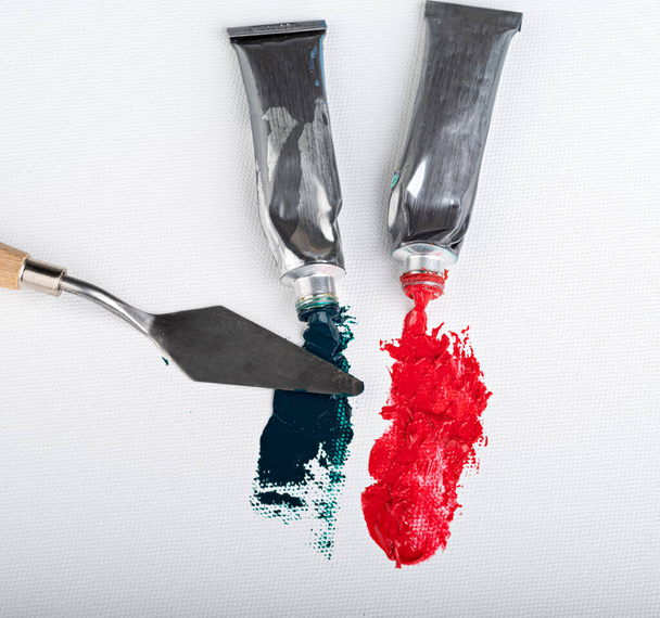 Смарагдова і червона олійна фарба течуть від трубок на полотні. Вид зверху
 - Фото, зображення