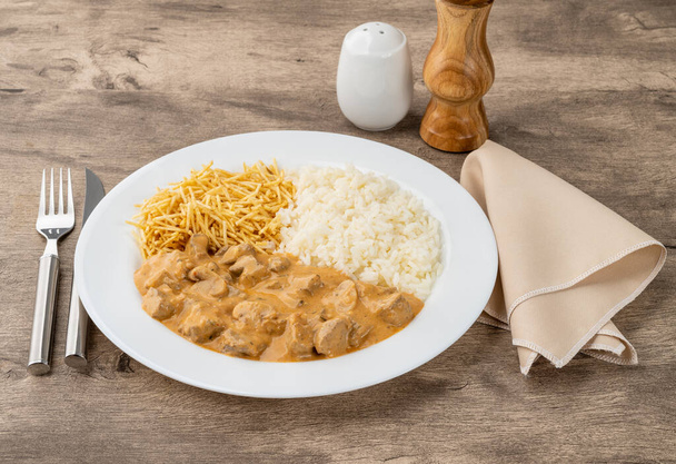 strogonoff de carne com arroz e palha de batata sobre mesa de madeira. - Foto, Imagem