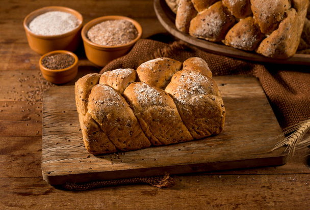 pan de pan hecho con semillas de sésamo (gergelim) en la mesa de madera rústica con otros panes e ingredientes en el fondo. - Foto, imagen