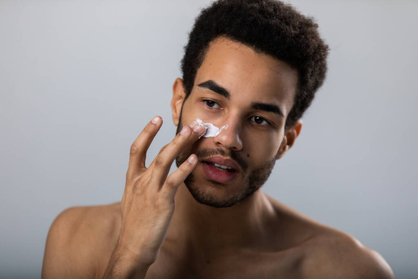 Young african american man applies moisturizer on his face. Male skin care. - Foto, Imagen