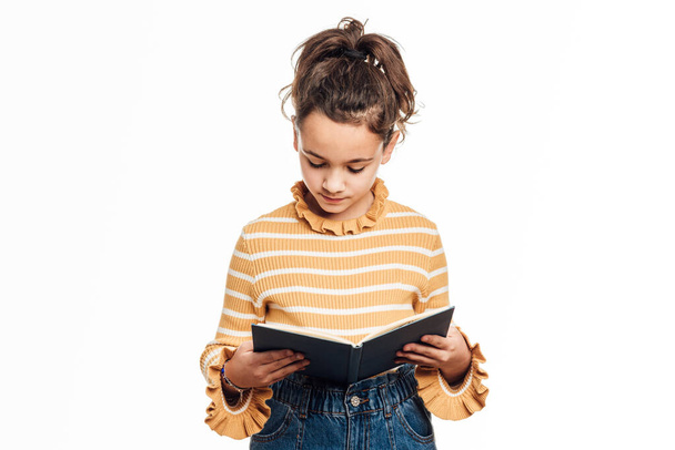 Chica joven leyendo un libro mientras está de pie sobre un fondo blanco aislado. - Foto, imagen
