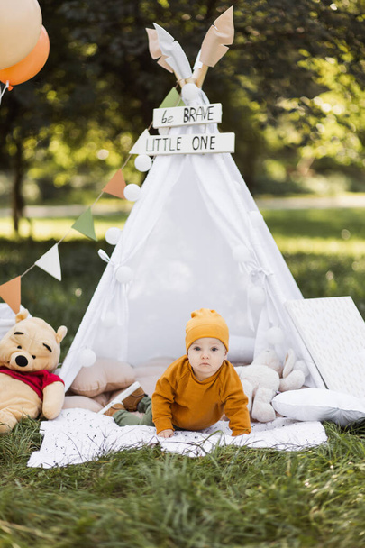Adorable boy sitting in wigwam with colorful toys outdoors - Фото, изображение