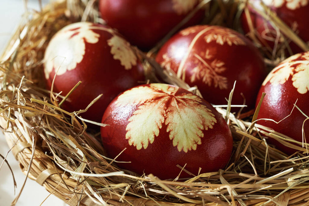 Пасхальные яйца, окрашенные луковой кожурой с рисунком свежих трав в плетеной корзине, закрыть - Фото, изображение