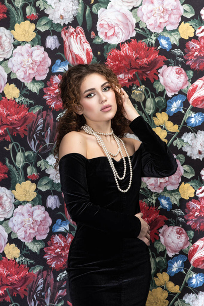 Beautiful model woman with curly hairstyle, background wall of flowers - 写真・画像