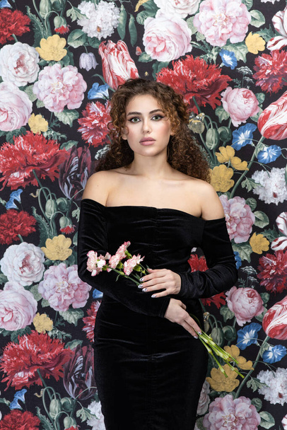 Beautiful model woman with curly hairstyle, background wall of flowers - Photo, Image