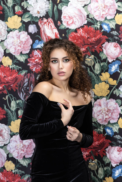 Beautiful model woman with curly hairstyle, background wall of flowers - Foto, Imagem