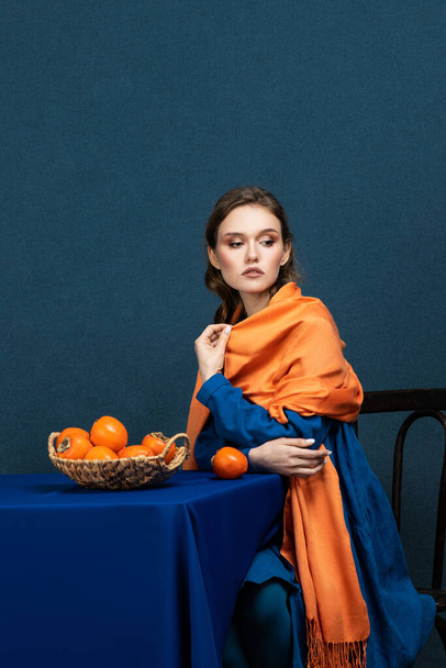 Stylish fashion young woman model, with evening make-up, posing in the studio, holding an exotic fruit in her hand. Photo on a dark blue background - Zdjęcie, obraz