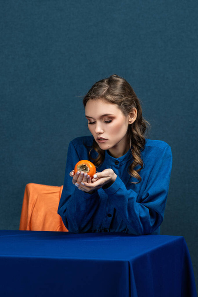 bright combination, a beautiful girl in a blue dress holds an orange persimmon  - Фото, зображення