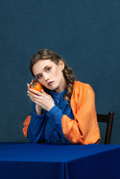 bright combination, a beautiful girl in a blue dress holds an orange persimmon  - Foto, immagini