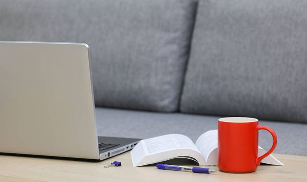 Kahvikuppi, kannettava tietokone ja kirja pöydällä sohvan lähellä - Valokuva, kuva