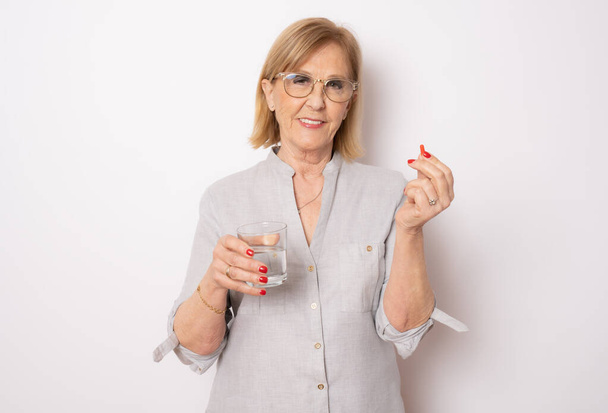 mujer mayor con vaso de agua y pastillas sobre fondo blanco - Foto, imagen