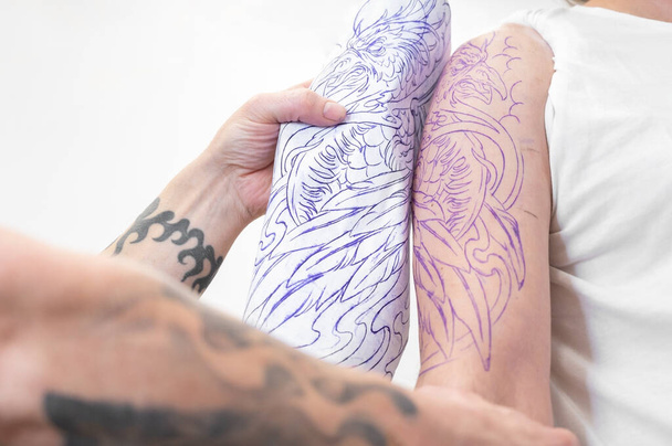 Geschickter Tätowierer legt Skizze auf den Arm eines Mannes. - Foto, Bild
