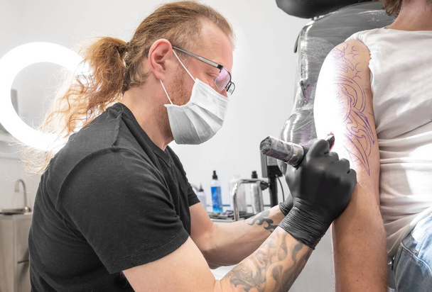 Tatuaggio con la sua macchina tatuare sul braccio con il disegno disegnato e con maschera protettiva contro covid 19, concetto di arte e design durante la nuova normale. - Foto, immagini
