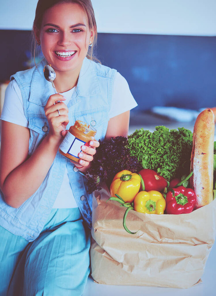 Young woman holding grocery shopping bag with vegetables .Standing in the kitchen - Фото, изображение